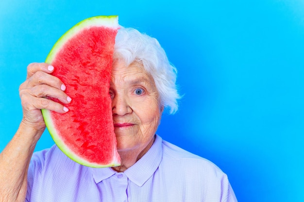 Reife Frau mit schneeweißen grauweißen Haaren im blauen Hemd mit Wassermelone im Studiohintergrund