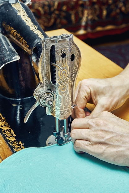 Reife Frau Schneiderin näht Blatt aus hellgrünem Stoff mit schwarzer Vintage-Werkzeugmaschine