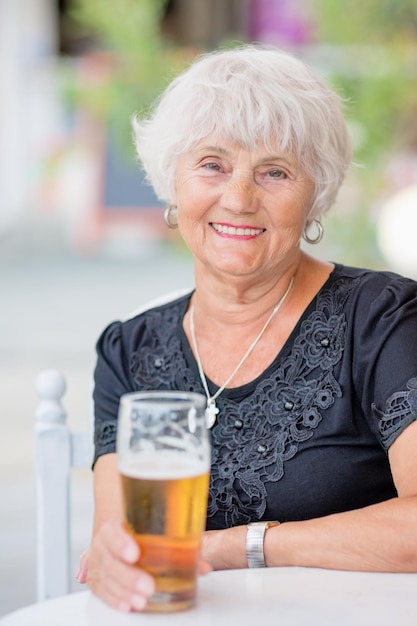 Foto reife frau sitzt an einem tisch in einem sommercafé und trinkt bier