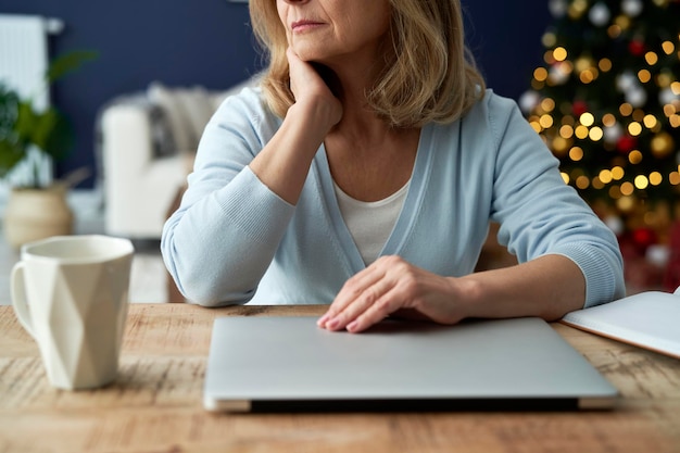 Reife Frau sitzt zu Weihnachten am Tisch mit Laptop