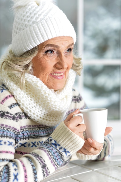 Foto reife frau trinkt tee, sitzt am fenster