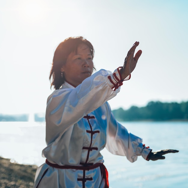 Foto reife frau übt am seeufer gegen den himmel kampfkünste aus