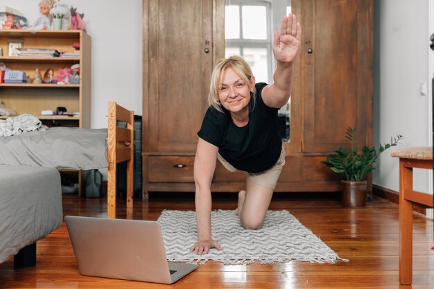 Reife Frau zu Hause beim Sportyoga auf dem Boden mit Laptop-Online-Kursen