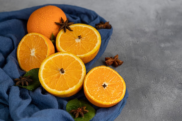 Reife frische Orangen in zwei Hälften geschnitten auf einem blauen Tuch. Mit Zimtstangen, Nelkensamen und grünen Blättern garniert.