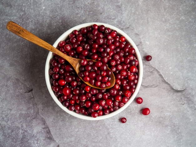 Reife frische Preiselbeeren in weißer Schüssel und Holzlöffel auf Betontischplatte mit Kopierraum