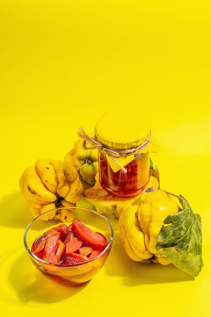 Reife ganze Quitte und süße Marmelade daraus isoliert auf gelbem Hintergrund. Frisches Obst, eine wesentliche Zutat für eine gesunde Ernährung, Dessert im Glas. Trendiges hartes Licht, dunkler Schatten, Kopierraum