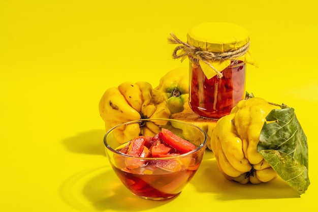 Reife ganze Quitte und süße Marmelade daraus isoliert auf gelbem Hintergrund. Frisches Obst, eine wesentliche Zutat für eine gesunde Ernährung, Dessert im Glas. Trendiges hartes Licht, dunkler Schatten, Kopierraum