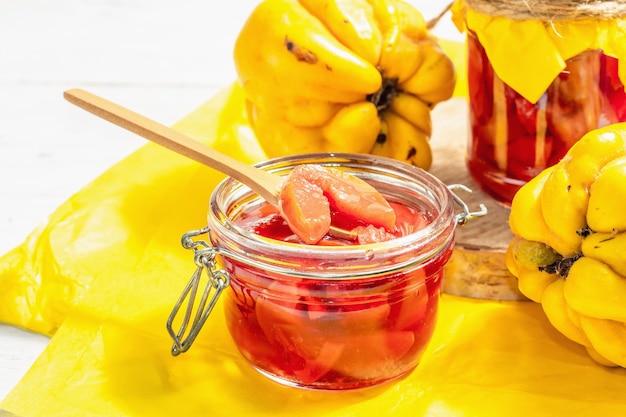 Reife ganze Quitten und süße Marmelade daraus. Frisches Obst, eine wesentliche Zutat für eine gesunde Ernährung, Dessert im Glas. Trendiges hartes Licht, dunkler Schatten. Weißer Holzhintergrund, Nahaufnahme