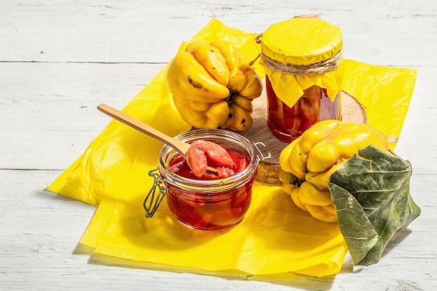 Reife ganze Quitten und süße Marmelade daraus. Frisches Obst, eine wesentliche Zutat für eine gesunde Ernährung, Dessert im Glas. Trendiges hartes Licht, dunkler Schatten. Weißer Holzhintergrund, Textfreiraum