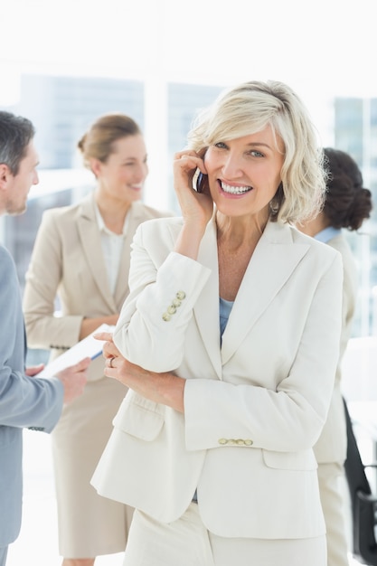 Reife Geschäftsfrau beim Anruf mit den Kollegen, die im Büro sich besprechen
