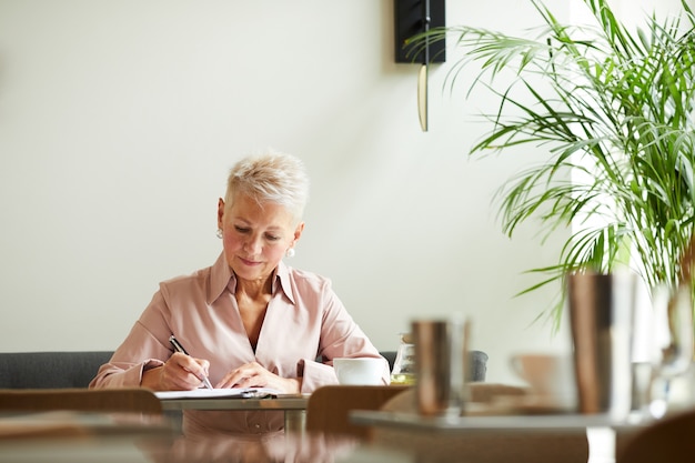 Reife Geschäftsfrau, die im Büro schreibt