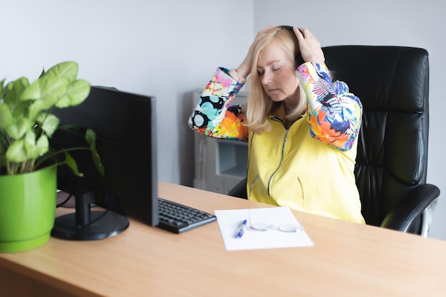 Reife Geschäftsfrau, die unter Kopfschmerzen vor dem Computer am Schreibtisch leidet