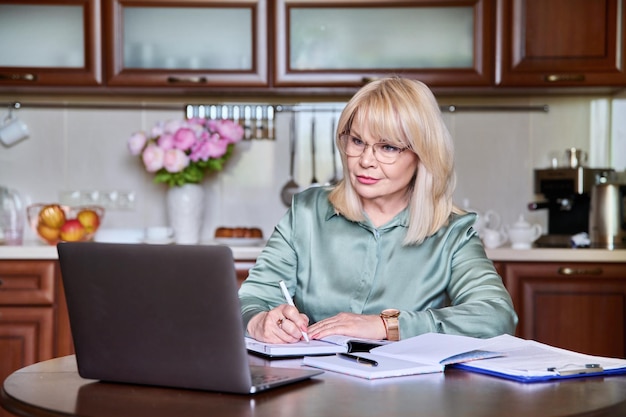 Reife Geschäftsfrau, die von zu Hause aus mit Laptop in der Küche arbeitet