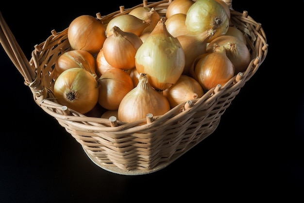 Reife goldene Zwiebel in einem Weidenkorb auf schwarzem Hintergrund