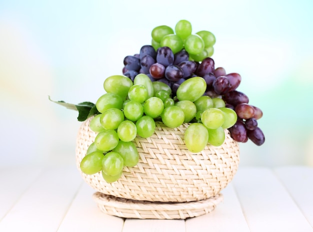 Reife grüne und violette Trauben im Korb auf Holztisch auf natürlichem Hintergrund