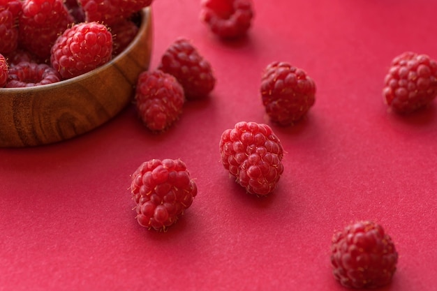 Foto reife himbeeren in einem holzbehälter auf rotem grund.