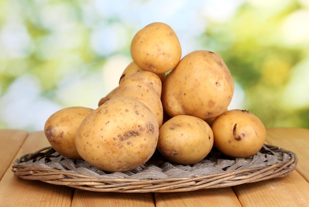 Reife Kartoffeln auf Korbwiege auf Holztisch auf natürlichem Hintergrund