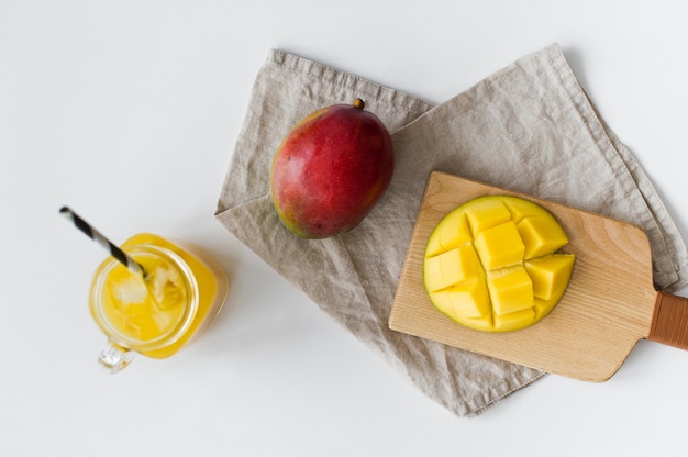 Reife Mango, halbe Mango und ein Glas Mangosaft auf einem hölzernen Schneidebrett.