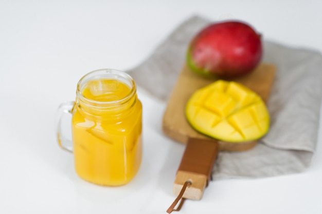 Reife Mango und ein Glas Mangosaft auf einem hölzernen Schneidebrett.