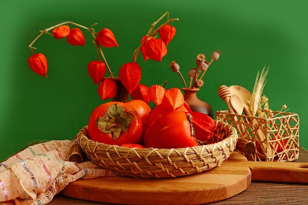 Reife orange Kaki des Stilllebens in einem dekorativen Tablett Blumensträuße von trockenen Pflanzen grüner Hintergrund Nahaufnahme