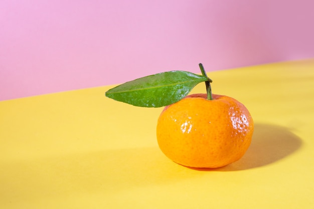 Foto reife orange mandarine mit blatt auf gelb und rosa in isometrischer