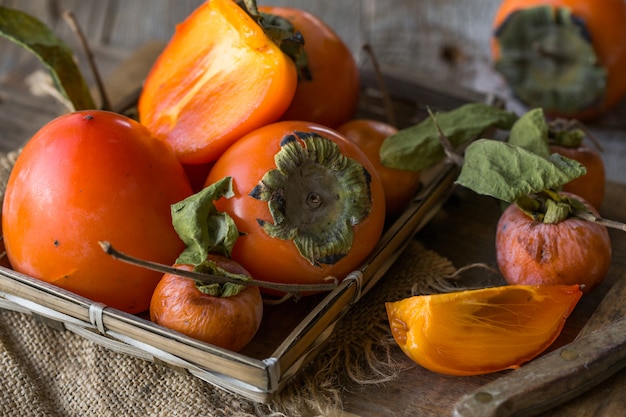 Reife Orangen-Kaki-Frucht. Kaki-Frucht auf Holztisch. Kakis-Scheiben. Kakis. Früchte von Kaki Persimmon (Diospyros kaki) im japanischen Herbst