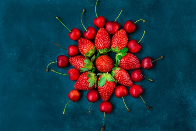 Reife organische Erdbeeren, glatte süße Kirschen vereinbarten in der Form der Blume, blauer Hintergrund