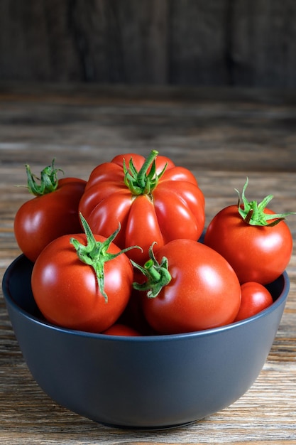 Reife organische rote Tomaten in einer Schüssel auf rustikalem Holztisch