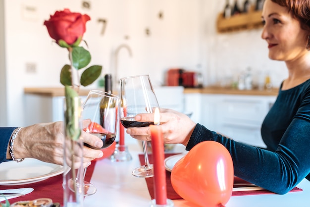 Reife Paare, die zu Hause romantisch für Valentinstag zu Abend essen und Toast mit Rotwein tun