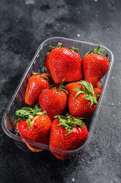 Reife rote Erdbeeren in Plastikverpackung auf Schwarz. Draufsicht