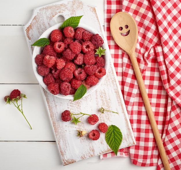 Reife rote Himbeeren in einer weißen hölzernen Platte auf einer Tabelle von Brettern