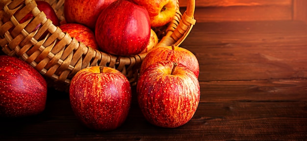 Reife rote Äpfel auf einem Holztisch, der aus einem Weidenkorb verschüttet wurde