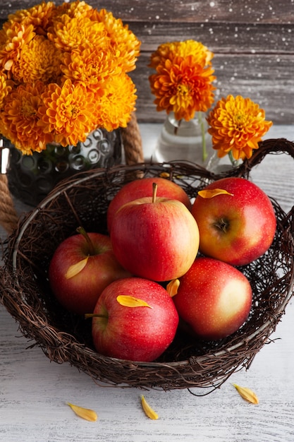 Reife rote Äpfel und gelbe Chrysantheme auf rustikalem Tisch. Herbstliches Dekor