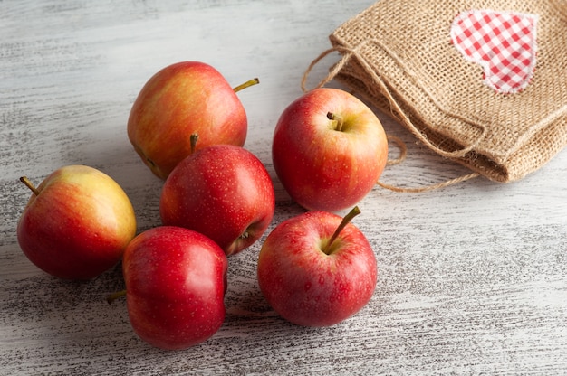 Reife rote Äpfel und Tasche mit Herz auf rustikalem Tisch. Herbstliches Rohkost