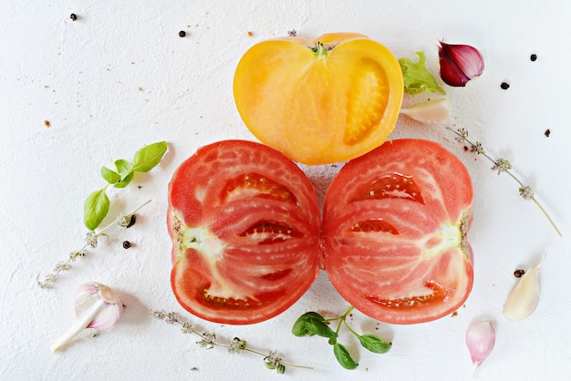 Foto reife rote und gelbe tomaten mit knoblauch-basilikum-thymian und gewürzen auf weißem grund