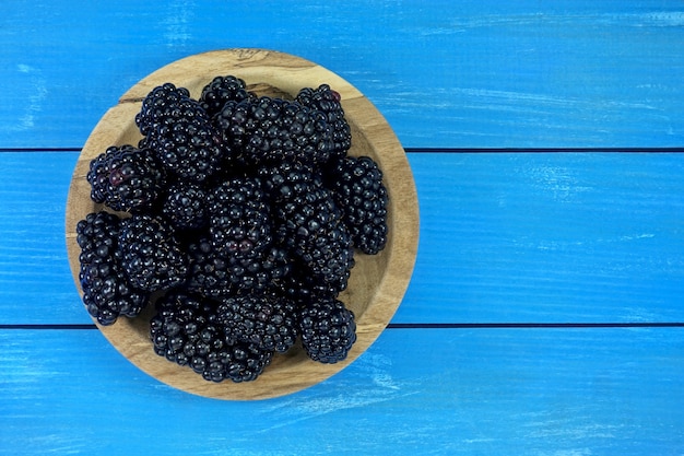 Reife schwarze Brombeeren auf einer Holzschale auf blauem Holzbretthintergrund, Ansicht von oben