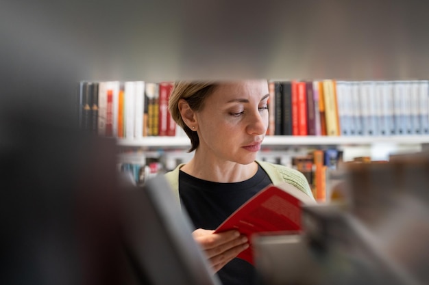 Foto reife studentin auf der suche nach einem buch im bücherregal der bibliothek, das auf dem campus der universität oder am college studiert