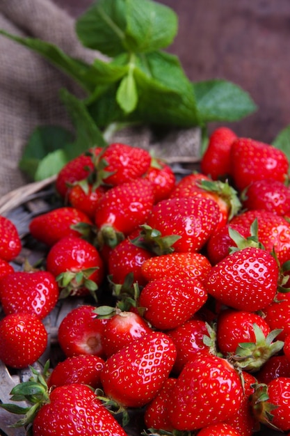 Reife süße Erdbeeren auf Weidenmatte auf farbigem Holzhintergrund