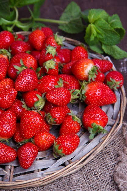 Reife süße Erdbeeren auf Weidenmatte auf farbigem Holzhintergrund