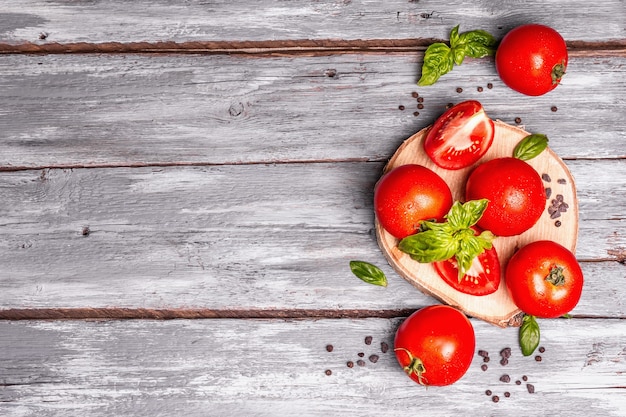 Reife Tomaten mit frischen Basilikumblättern, schwarzem Salz und Pfefferkörnern. Ganzes und geschnittenes halbes Gemüse, alter Holzbretthintergrund, Draufsicht