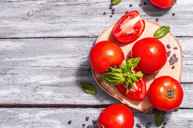 Reife Tomaten mit frischen Basilikumblättern, schwarzem Salz und Pfefferkörnern. Ganzes und halb geschnittenes Gemüse, trendiges hartes Licht, dunkler Schatten. Alte Holzbretter Hintergrund, Ansicht von oben