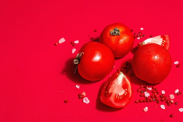 Reife Tomaten mit rosa Himalaya-Salz und rosa Pfeffer. Ganzes und halb geschnittenes Gemüse, trendiges hartes Licht, dunkler Schatten, roter kulinarischer Hintergrund, Kopierraum