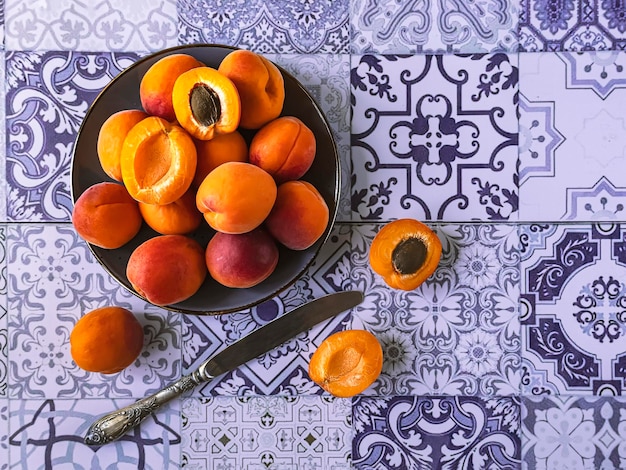 Reife und geschnittene orangefarbene Aprikosen mit grünen Blättern auf einem Teller auf blauem Hintergrund, Vintage-Messer