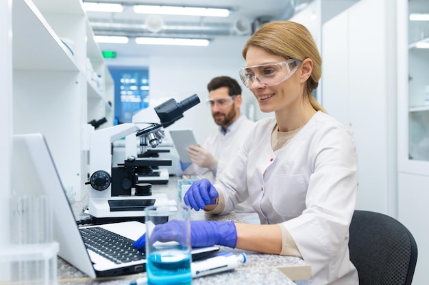 Reife Wissenschaftlerin im weißen Kittel bei der Arbeit Laborassistentin mit Mikroskop und Laptop an