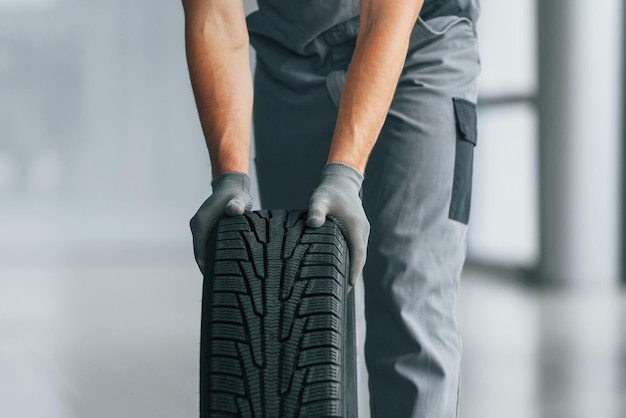 Reifen auf dem Boden Mann in Uniform arbeitet tagsüber im Autosalon