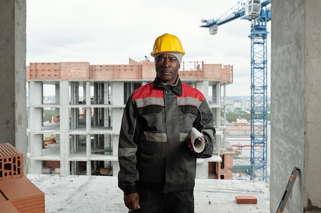Reifer afrikanisch-amerikanischer Baumeister mit gerolltem Bauplan, der in die Kamera blickt