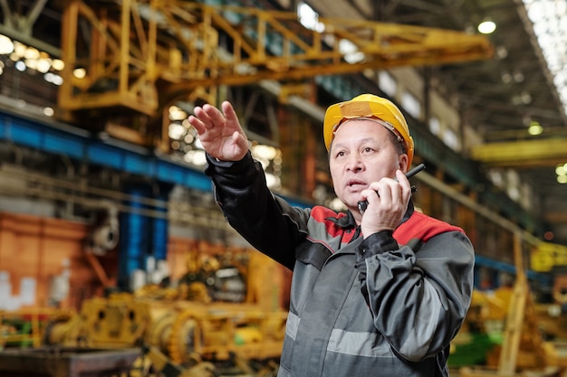 Reifer Arbeiter im Helm mit Sender bei seiner Arbeit in der Fabrik