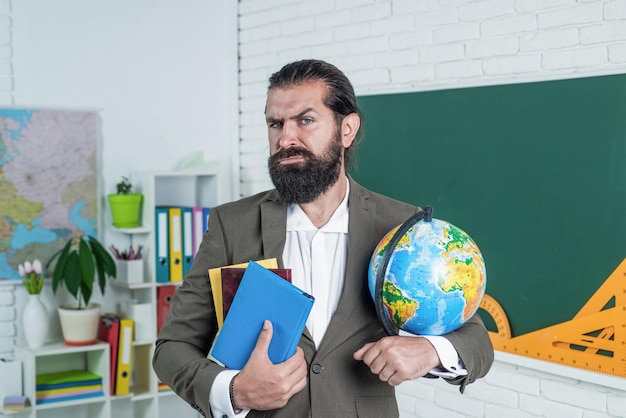 reifer bärtiger mann lehrer in kostüm sitzt im schulklassenzimmer mit geographie-globuskarte, reise.