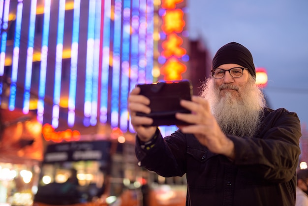 Reifer bärtiger Touristenmann, der Foto mit Telefon in Chinatown bei Nacht macht