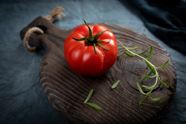 Reifer Bio-Tomaten-Rosmarin-Zweig auf einem alten Schneidebrett